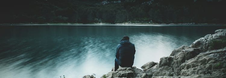 person sitting alone at the edge of a lake