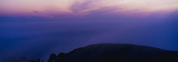 person in the far distance on a hill beneath purple sky