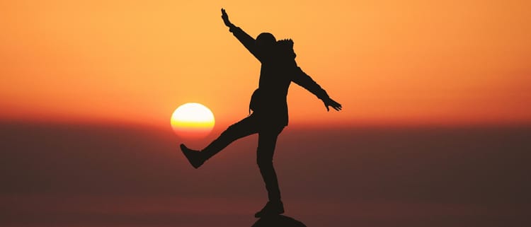 person balancing on a rock joyously but dangerously