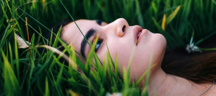 female lying in long grass looking pensively up towards the sky