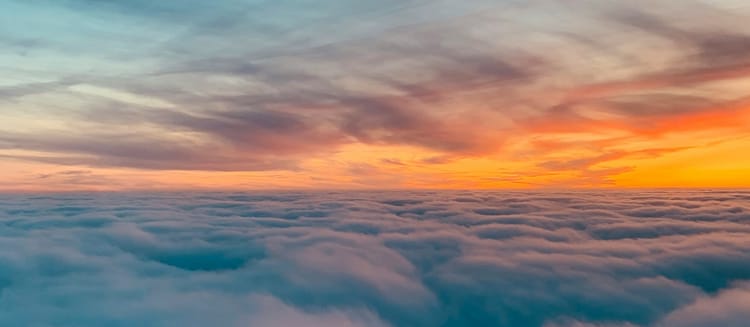 above the clouds during a glowing orange sunrise