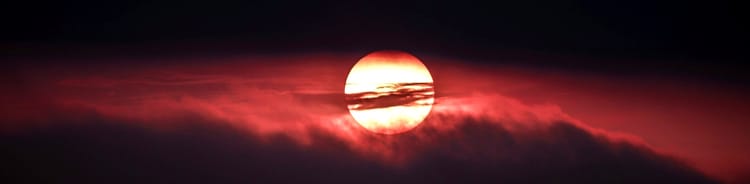 rising or setting sun surrounded by clouds with a red glow over the whole scene