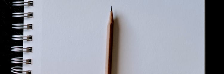 sharpened wooden pencil lying on an open notebook page that is blank