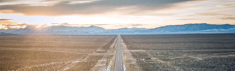 long straight road cutting through empty fields towards distant mountains