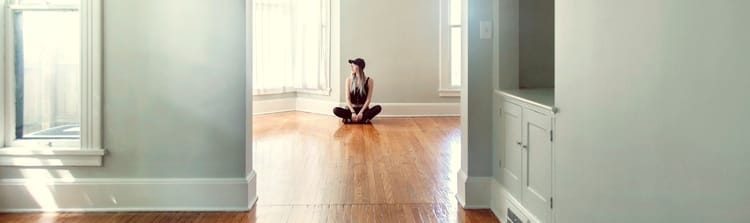 person sitting alone on the floor in a house completely empty of furnishings