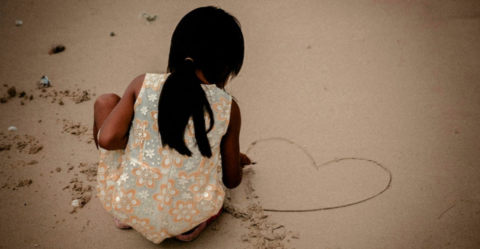 child drawing heart shape in the sand at the seashore