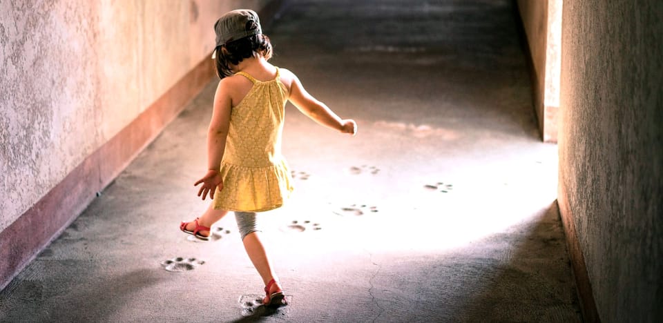 young girl walking down a hallway following footprints on the ground