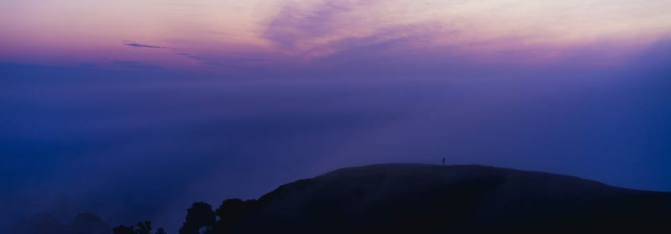 person in the far distance on a hill beneath purple sky