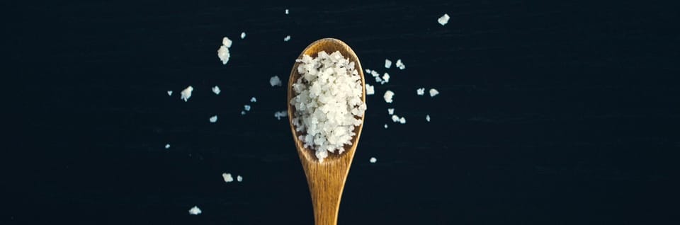 wooden spoon full of course salt flakes with some spilled out onto a tabletop