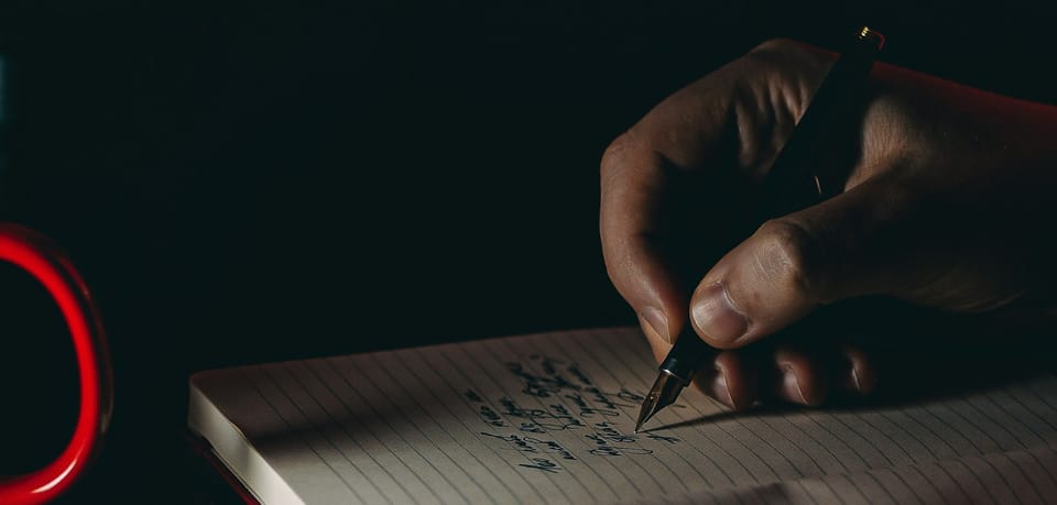 person writing in a notebook with a fountain pen at night