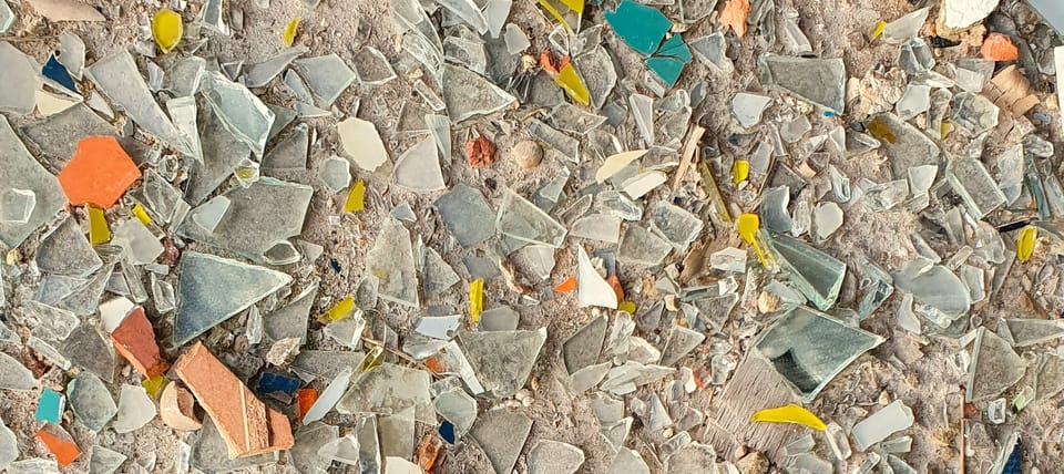 many shards of broken colorful glass strewn on a sandy beach